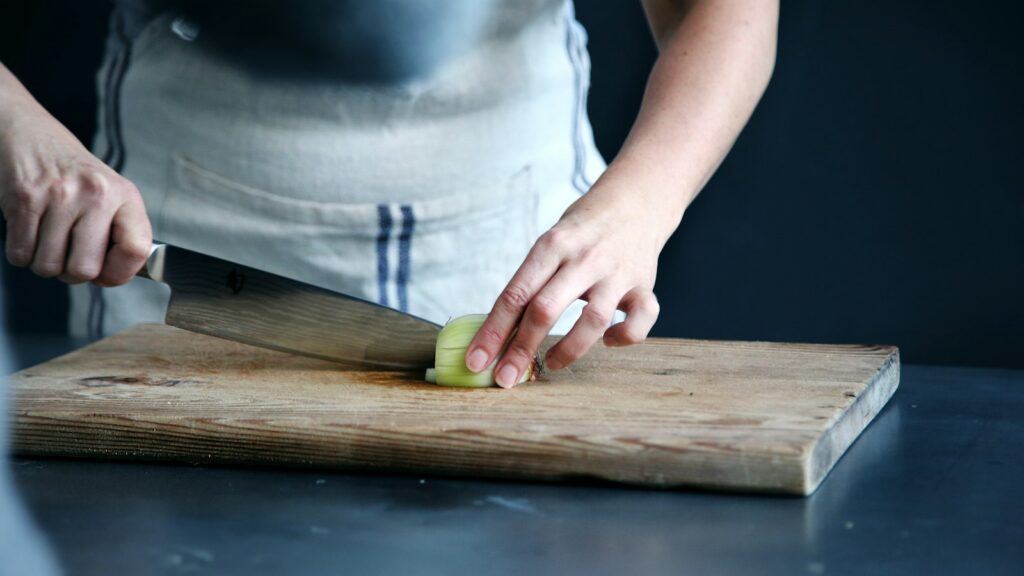 A person slicing vegetables on a wooden board in a kitchen.